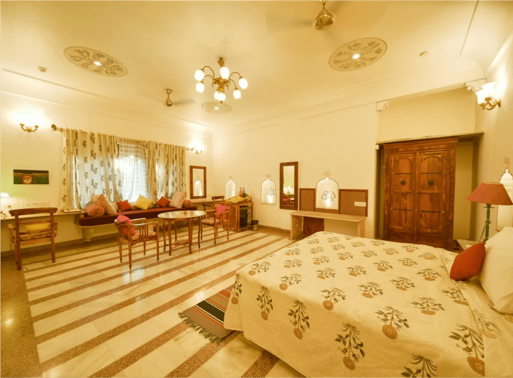 A heritage suite at Dera Mandawa featuring a scalloped archway, traditional Rajasthani decor, and a hand-painted ceiling, reflecting the slow travel in Jaipur's experience of a palace stay.