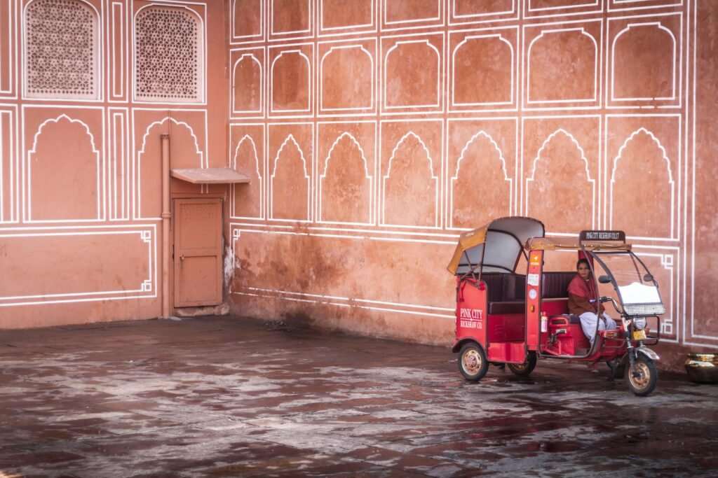 Discover Jaipur in Summer: Off-Season Charm and Heritage Stays at Dera Mandawa 4 A woman driving a red "Pink City Rickshaw Co." tuk-tuk. City Palace of Jaipur, often called the "Pink City".