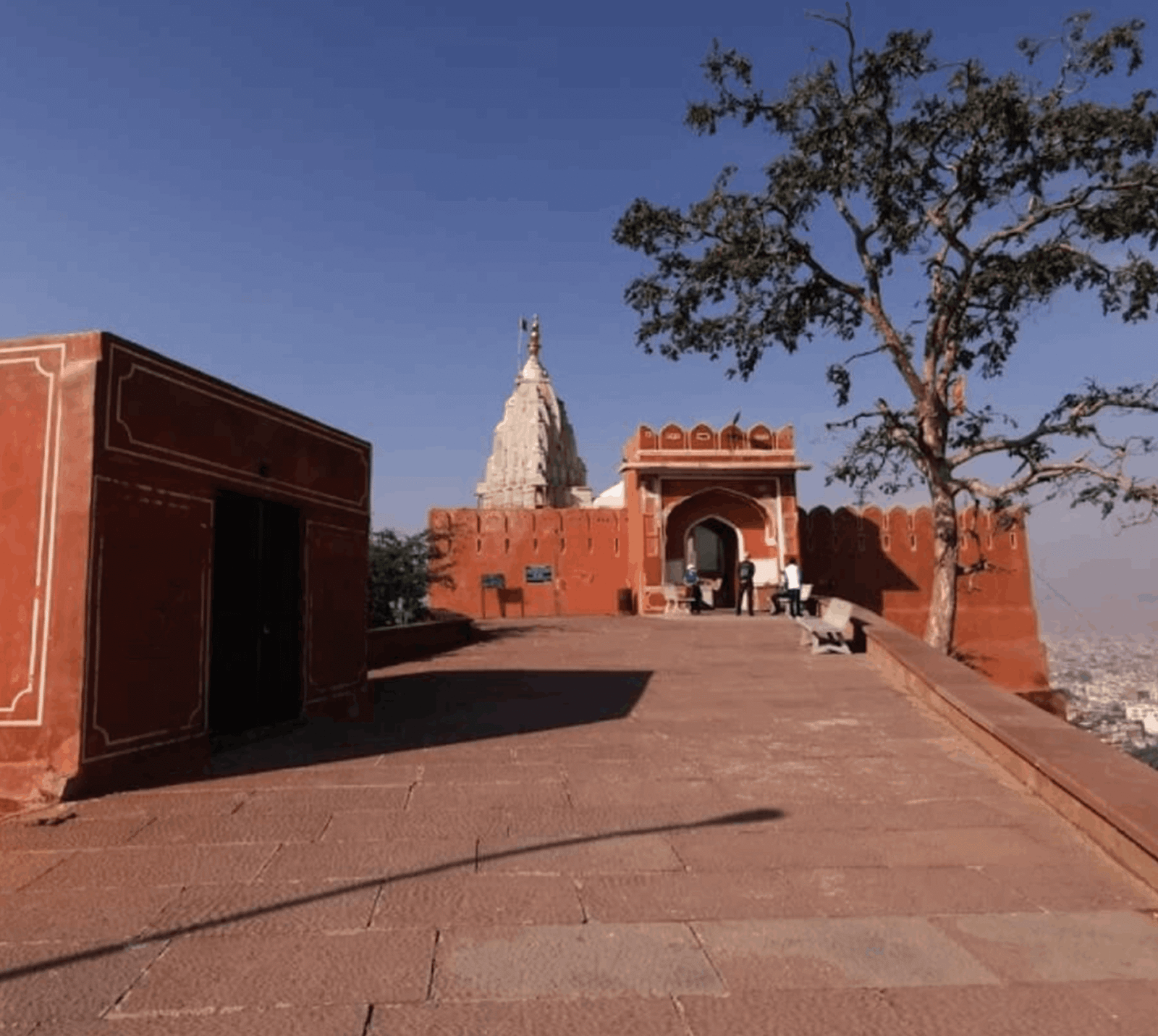 White shikhara of Surya Mandir rising behind red sandstone walls and an arched gateway on the hilltop above Galtaji in Jaipur