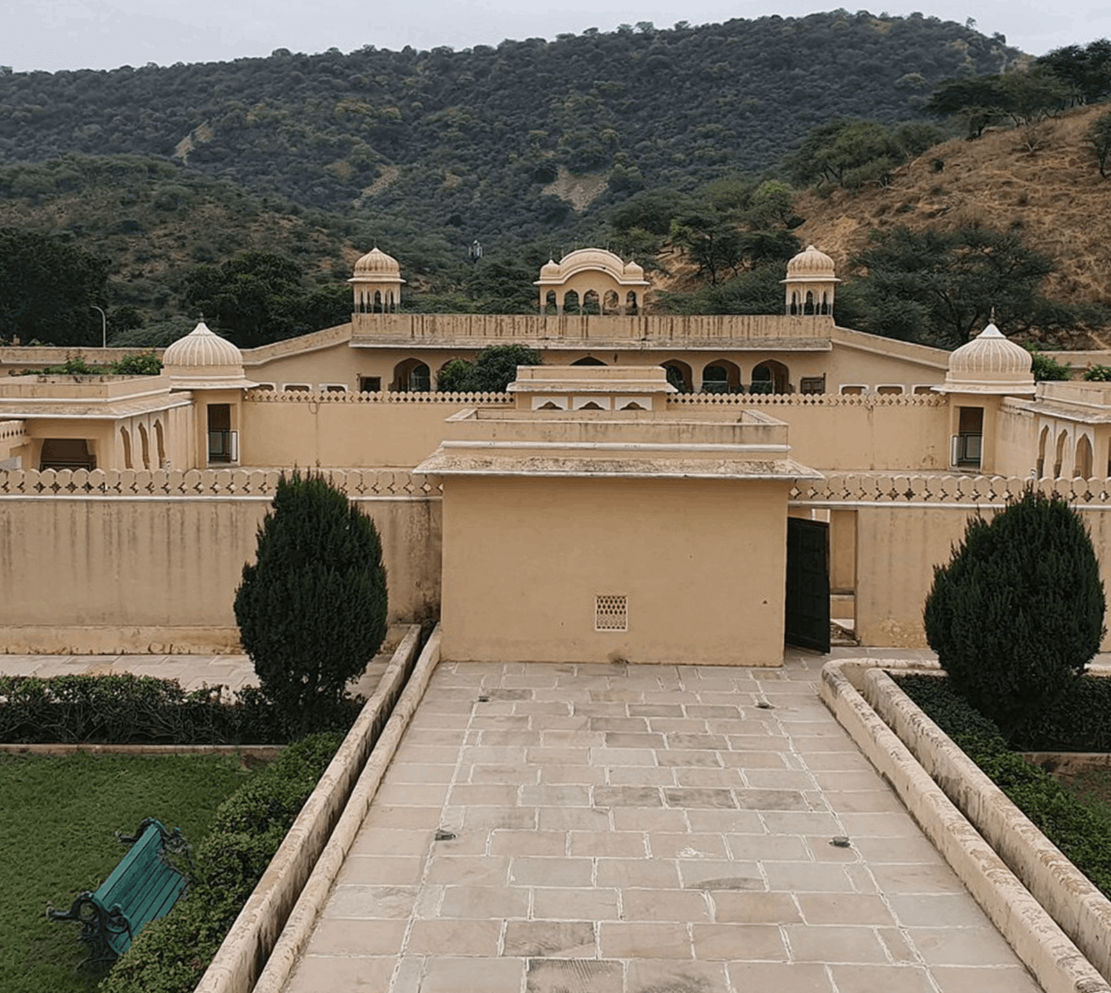 Stone pathway leading to the sandstone walls, chhatris and pavilions of Vidyadhar Garden set against green Aravalli hills in Jaipur