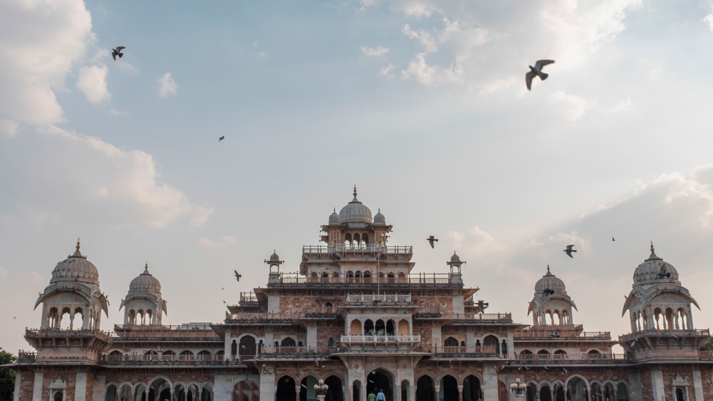 Albert Hall Museum in Jaipur with domed towers and pigeons flying above under a cloudy sky